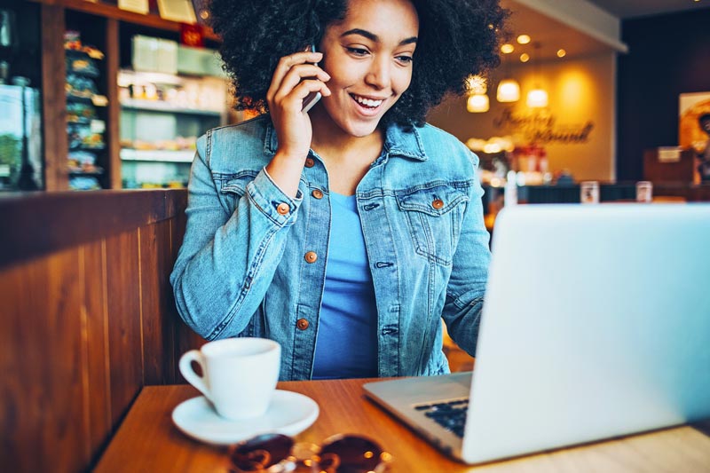 Girl in a jean jacket on her phone at her laptop