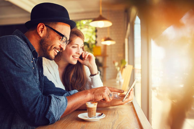Happy couple sitting at a coffee bar looking at their mobile phone