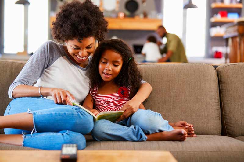 Mother and daughter snuggled on a couch reading a book