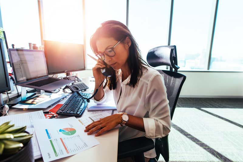 A woman wearing glasses at her desk and studying documents